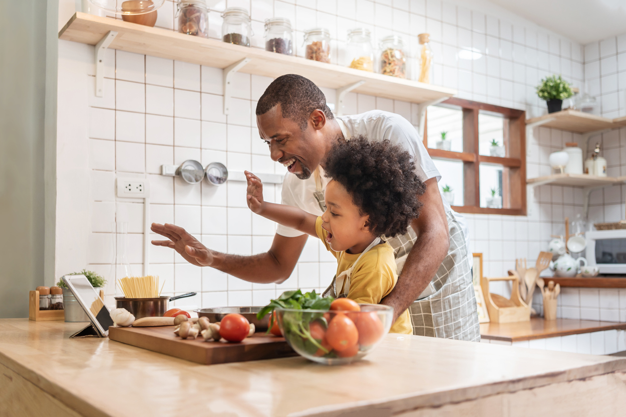 Father and son cooking together in bright kitchen on a video call