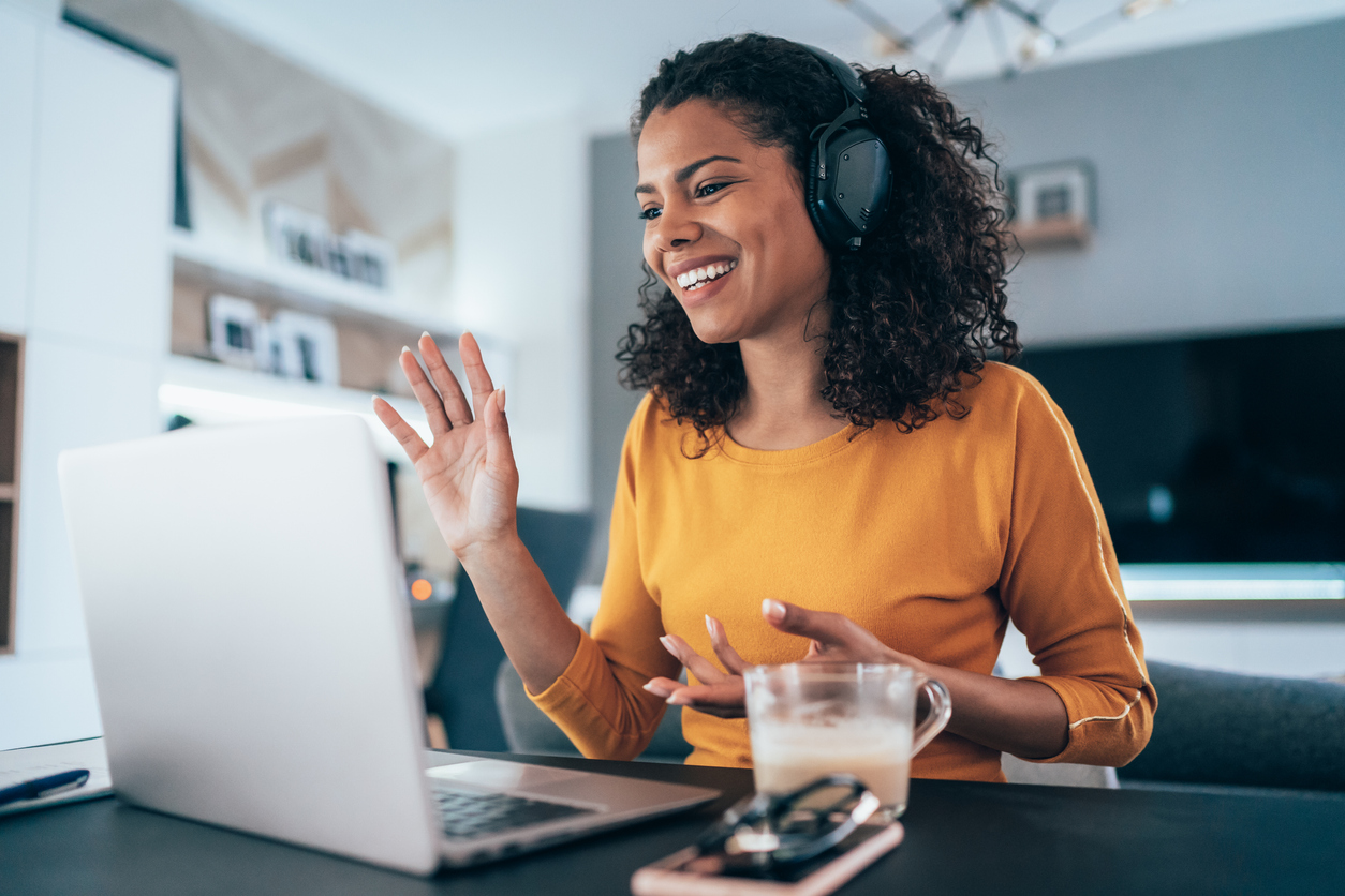 Woman with headphones waving at computer